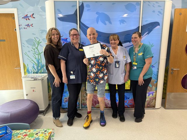 A donor presenting a certificate to Pod with play staff and entertainer at a children's ward